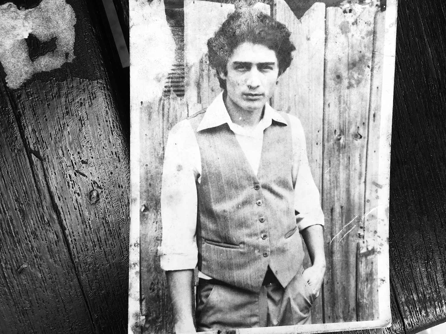 Close-up in black and white of a photograph of Gheorghe when he was younger. He is wearing a white shirt and jacket and his left hand is in his pocket.